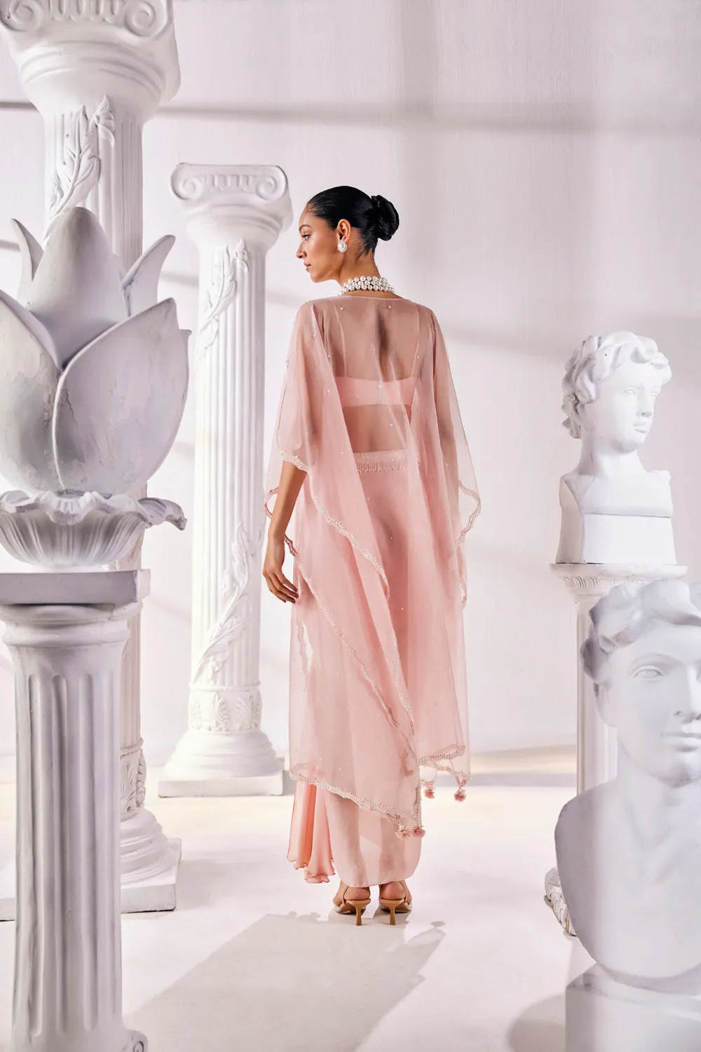 Peach Draped Skirt In Satin Georgette Paired With A Belt And A Pearl Detailed Blouse With A Soft Organza Cape.